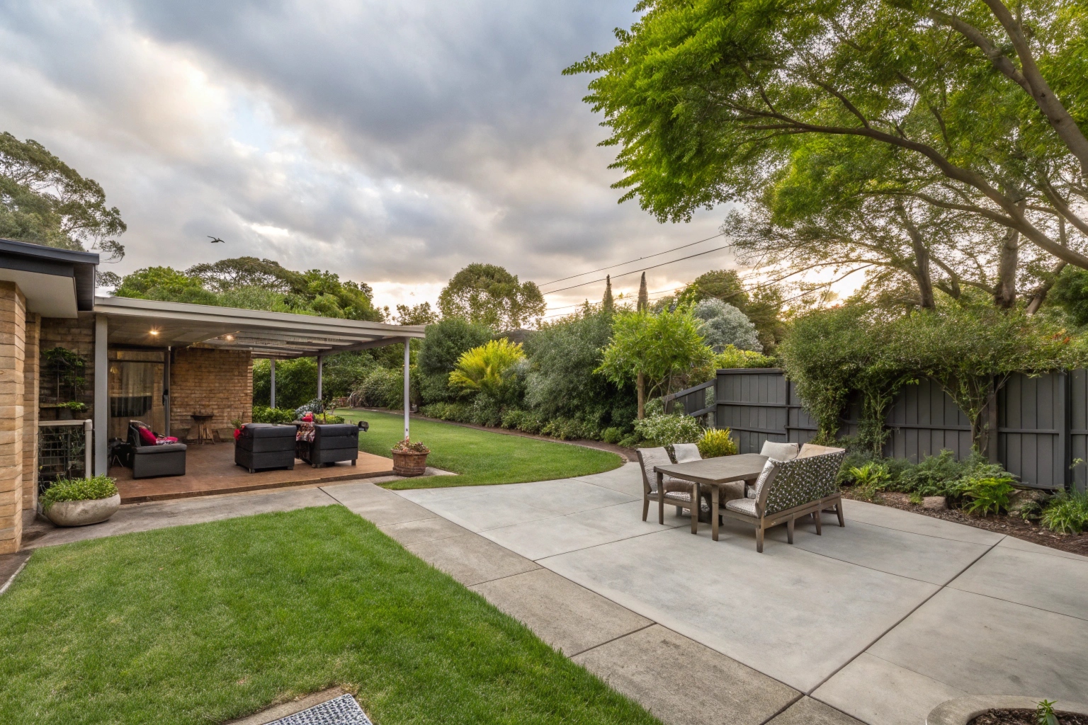 An attractive concrete patio area in a Macgregor home backyard with outdoor furniture, surrounded by greenery and shade trees, family entertaining space
